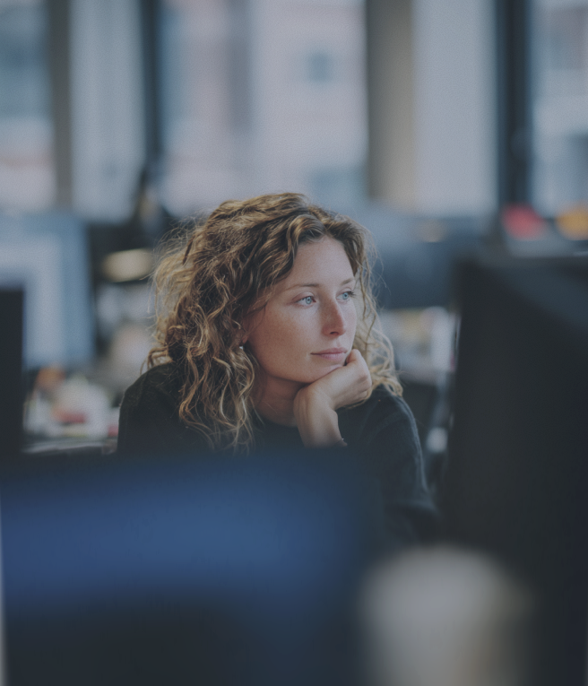 A woman with curly hair gazes thoughtfully in an office setting.