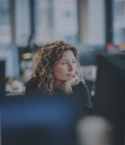 A woman with curly hair gazes thoughtfully in an office setting.
